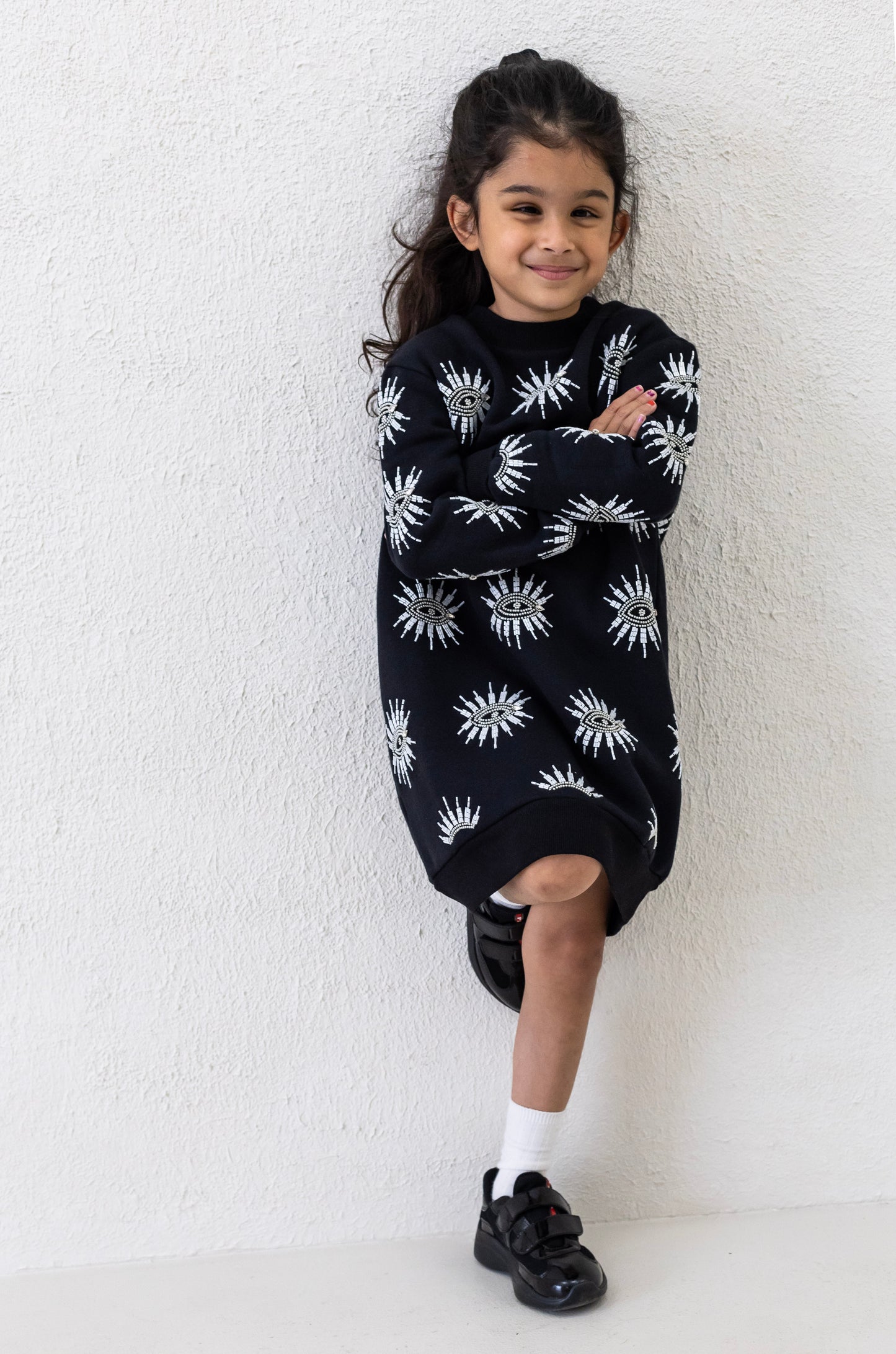 Little girl wearing a sustainably and ethically handcrafted black sweatshirt dress with a beaded eye pattern.