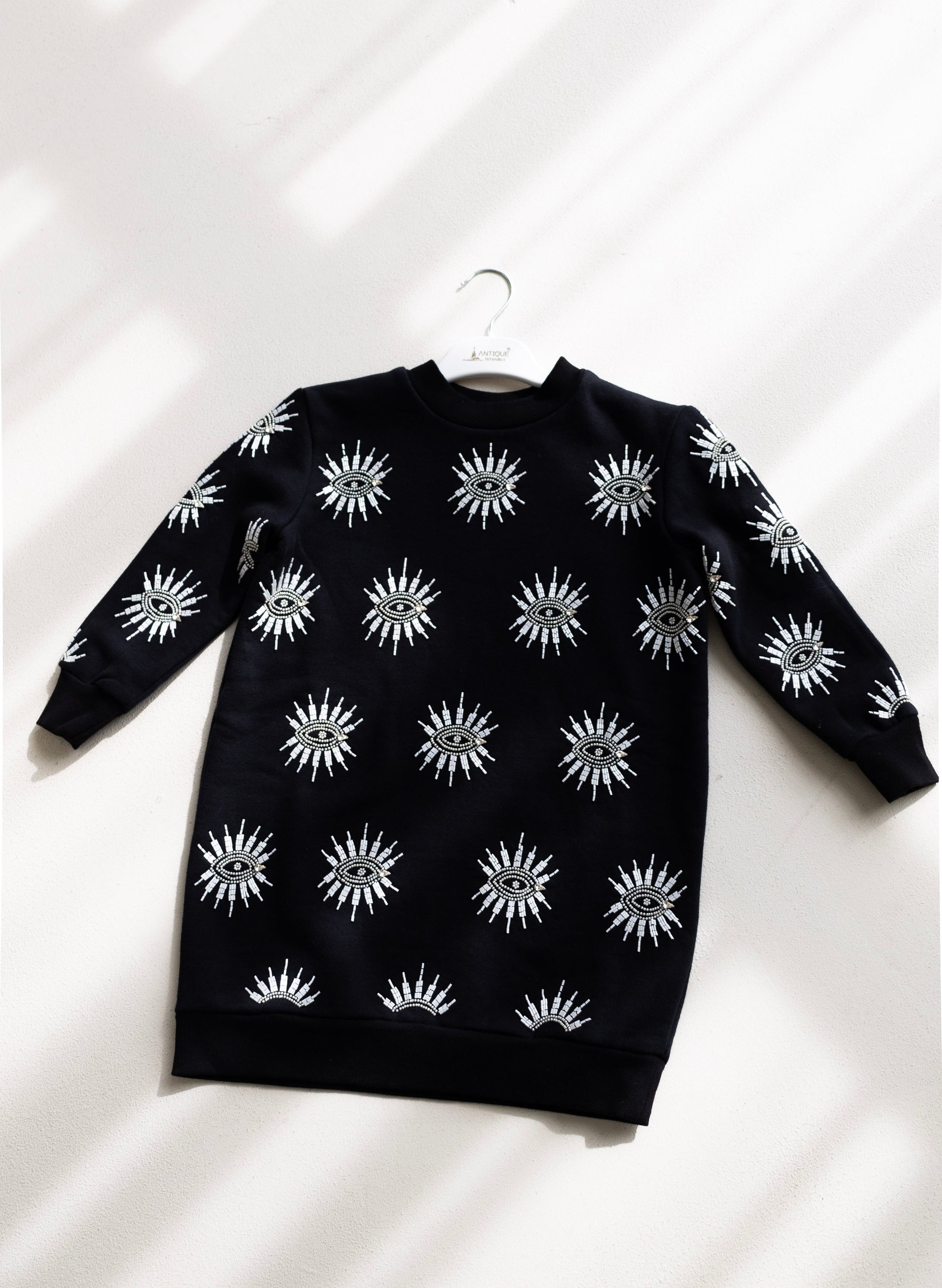 Sustainably and ethically handcrafted black kids sweatshirt dress with a white beaded eye pattern.