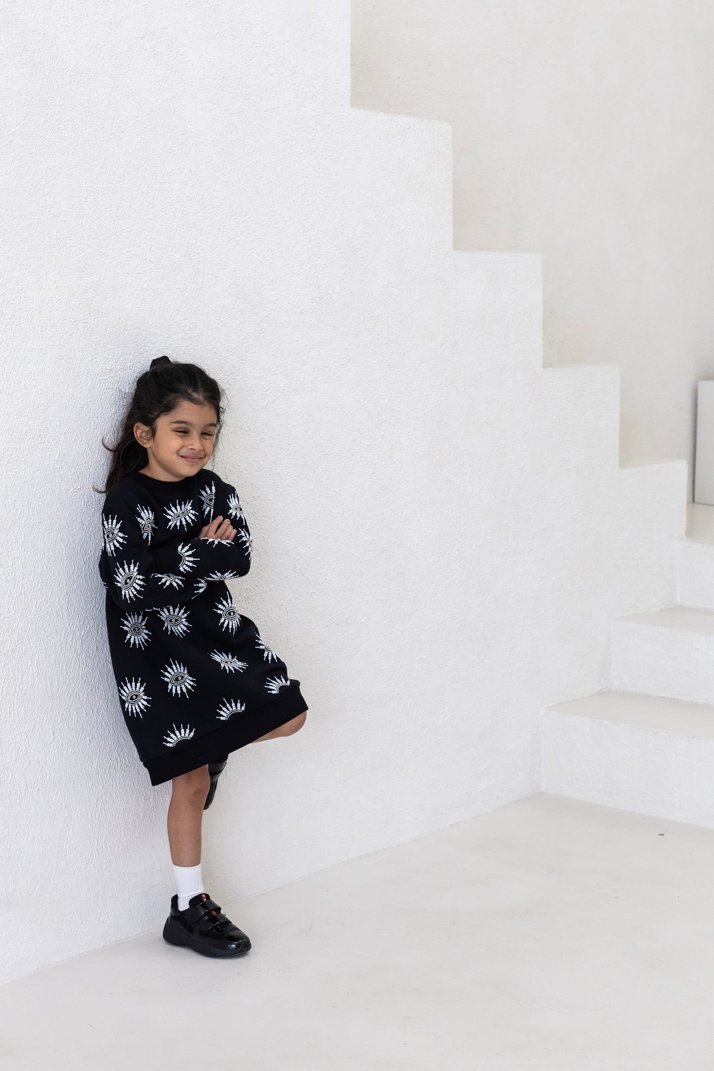 Little girl wearing a sustainably and ethically handcrafted black sweatshirt dress with a beaded eye pattern.