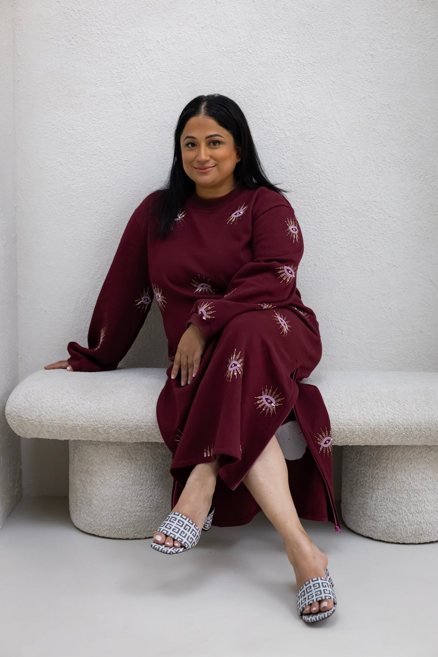 Woman wearing a sustainably and ethically handcrafted burgundy sweatshirt dress with a beaded eye pattern.