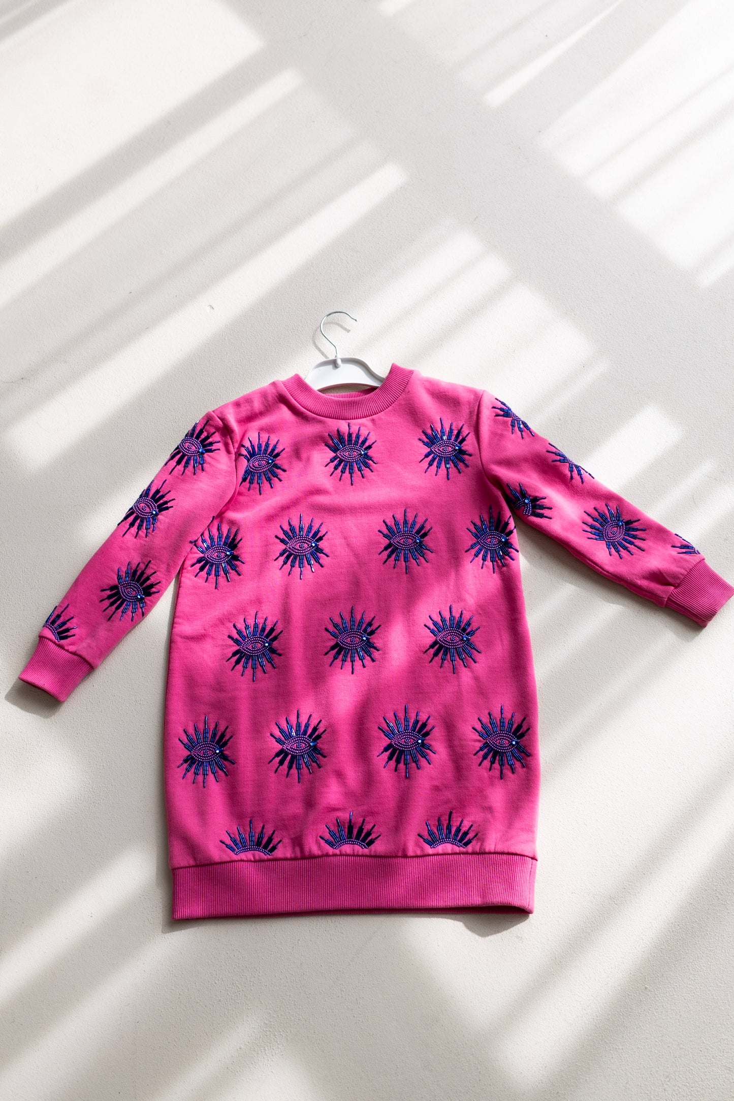 Sustainably and ethically handcrafted pink kids sweatshirt dress with a blue beaded eye pattern.