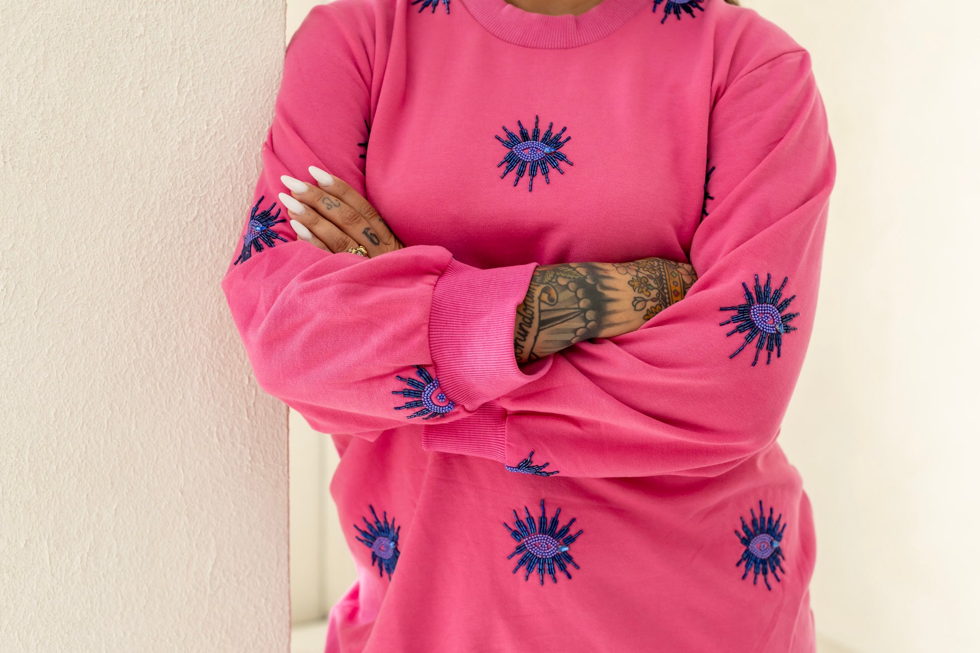 Woman wearing a sustainably and ethically handcrafted pink sweatshirt dress with a blue beaded eye pattern.