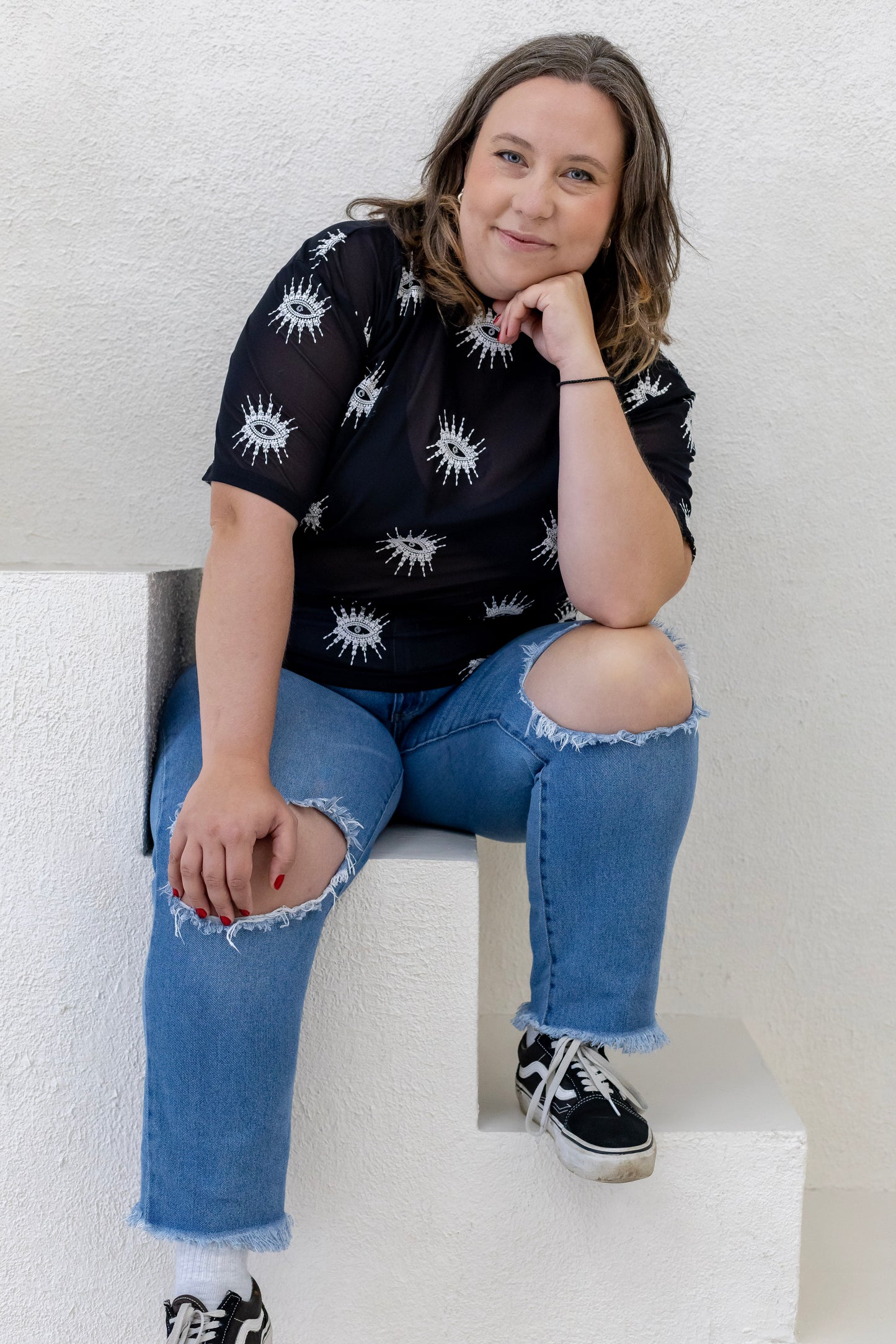 Woman wearing a sustainably and ethically handcrafted sheer black shirt with a white embroidered eye pattern.