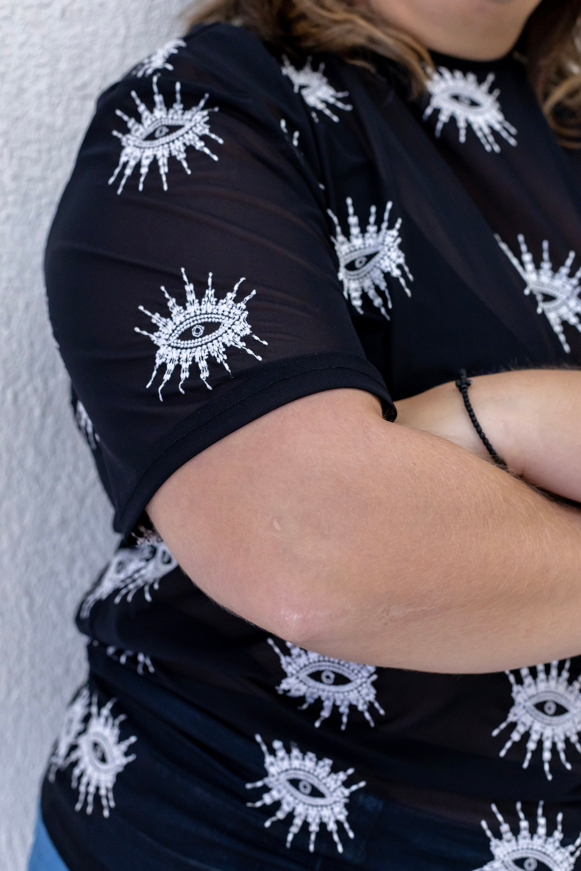 Woman wearing a sustainably and ethically handcrafted sheer black shirt with a white embroidered eye pattern.