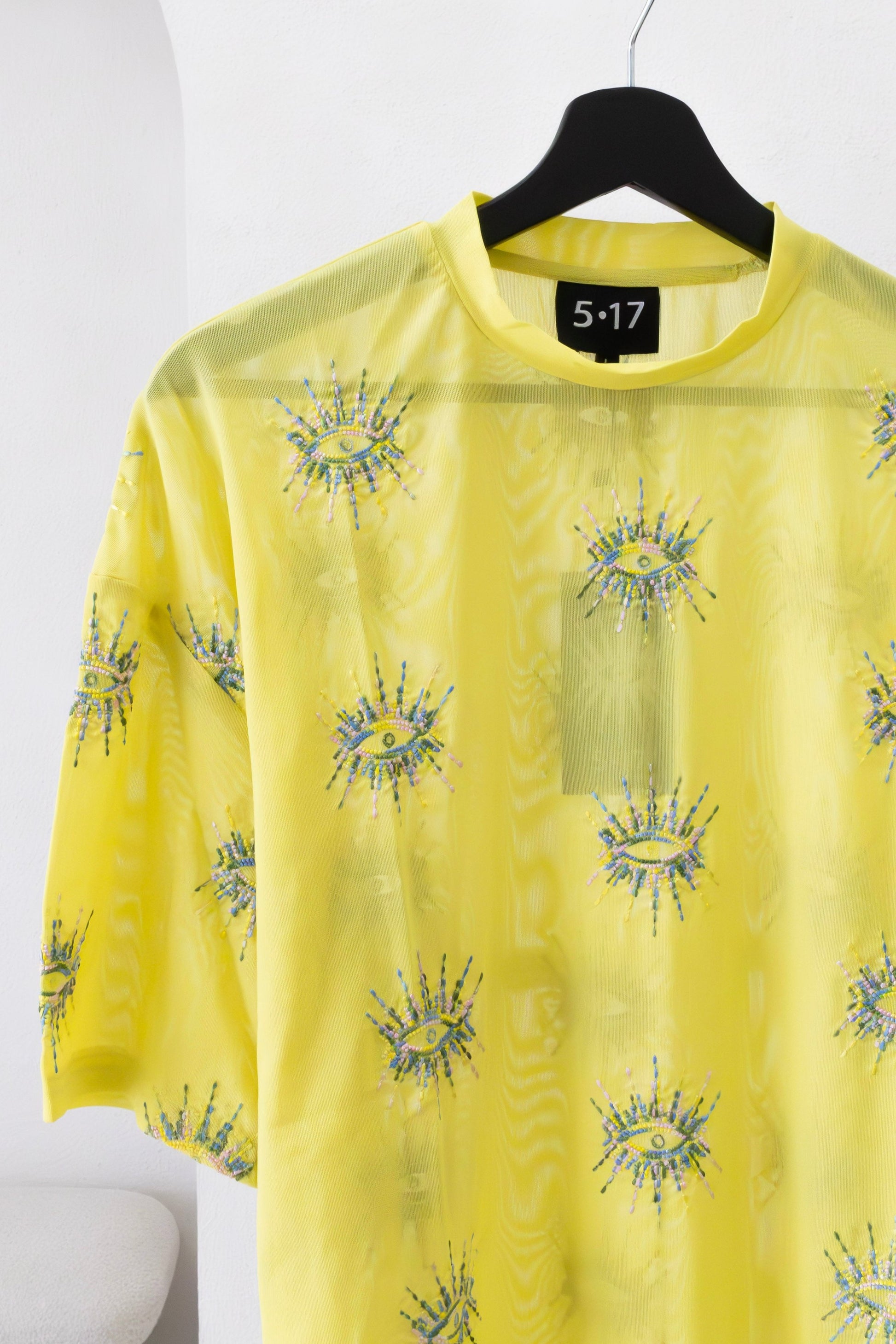 Woman wearing a sustainably and ethically handcrafted sheer yellow shirt with a white embroidered eye pattern.