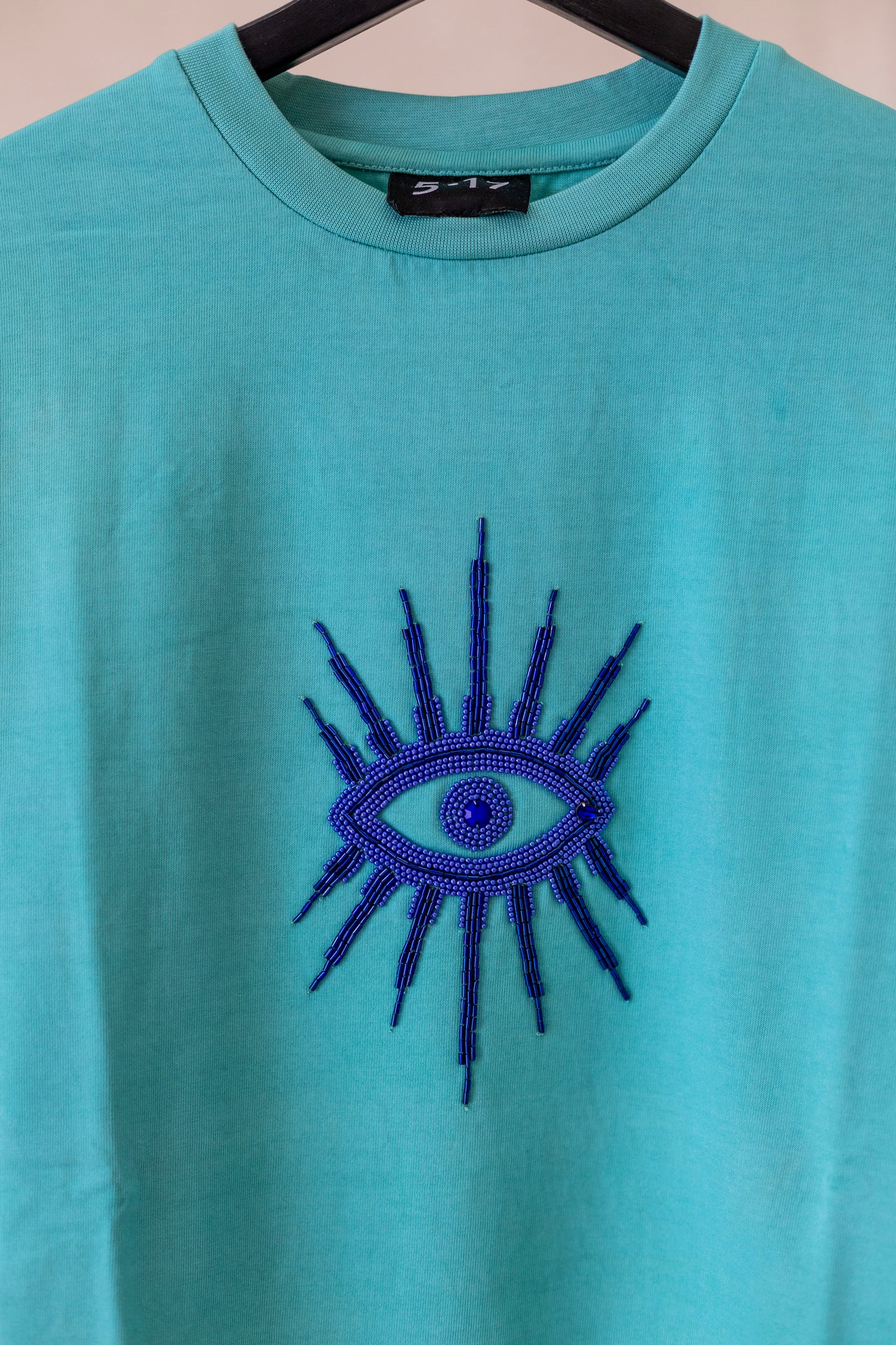 Sustainably and ethically handcrafted teal shirt with a blue beaded eye.