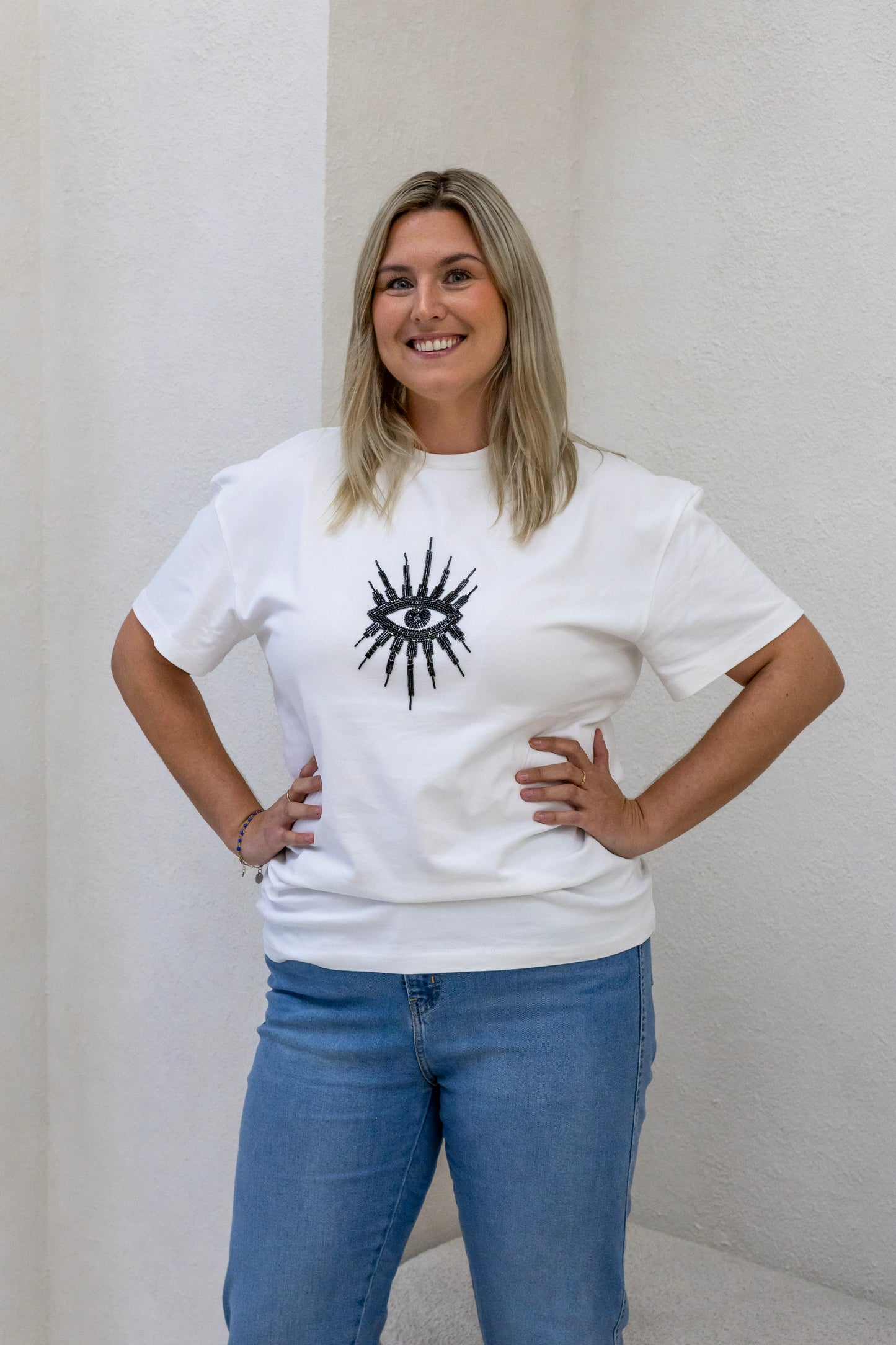 Woman wearing a sustainably and ethically handcrafted white t-shirt with a black beaded eye pattern.